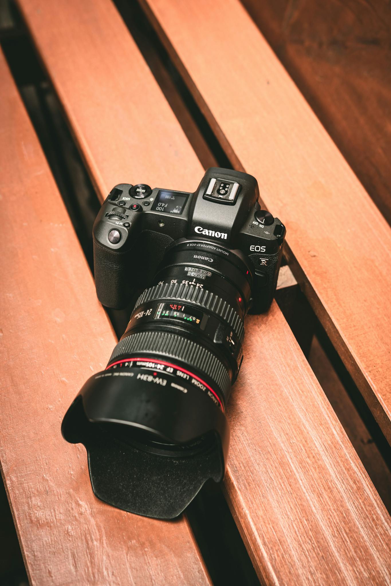 Close-up of a Canon DSLR camera resting on a wooden bench with focus on lens and details.