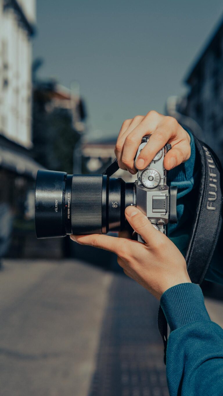 Close-up shot of a person holding a professional camera, capturing an urban scene.