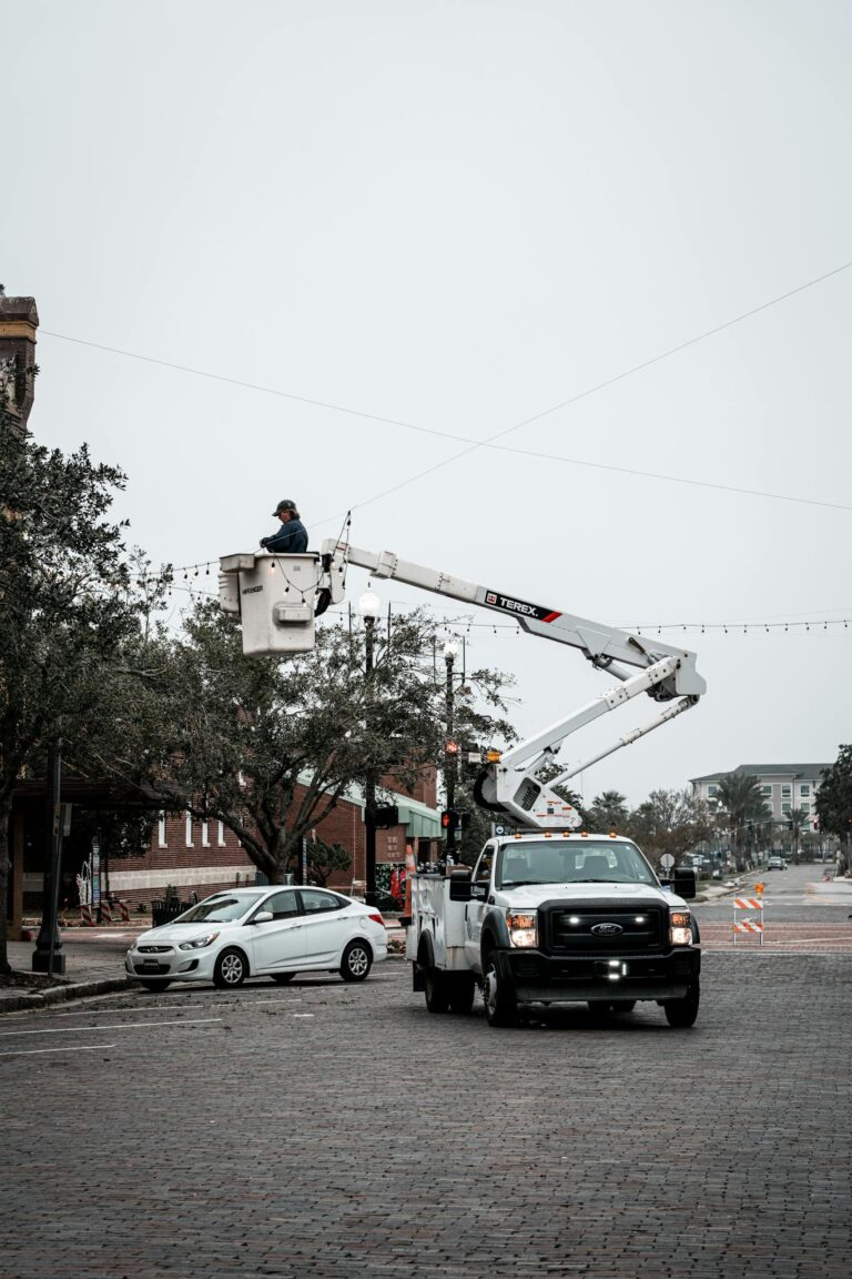 Urban streetscape with city workers fixing streetlights using a cherry picker truck on an overcast day.